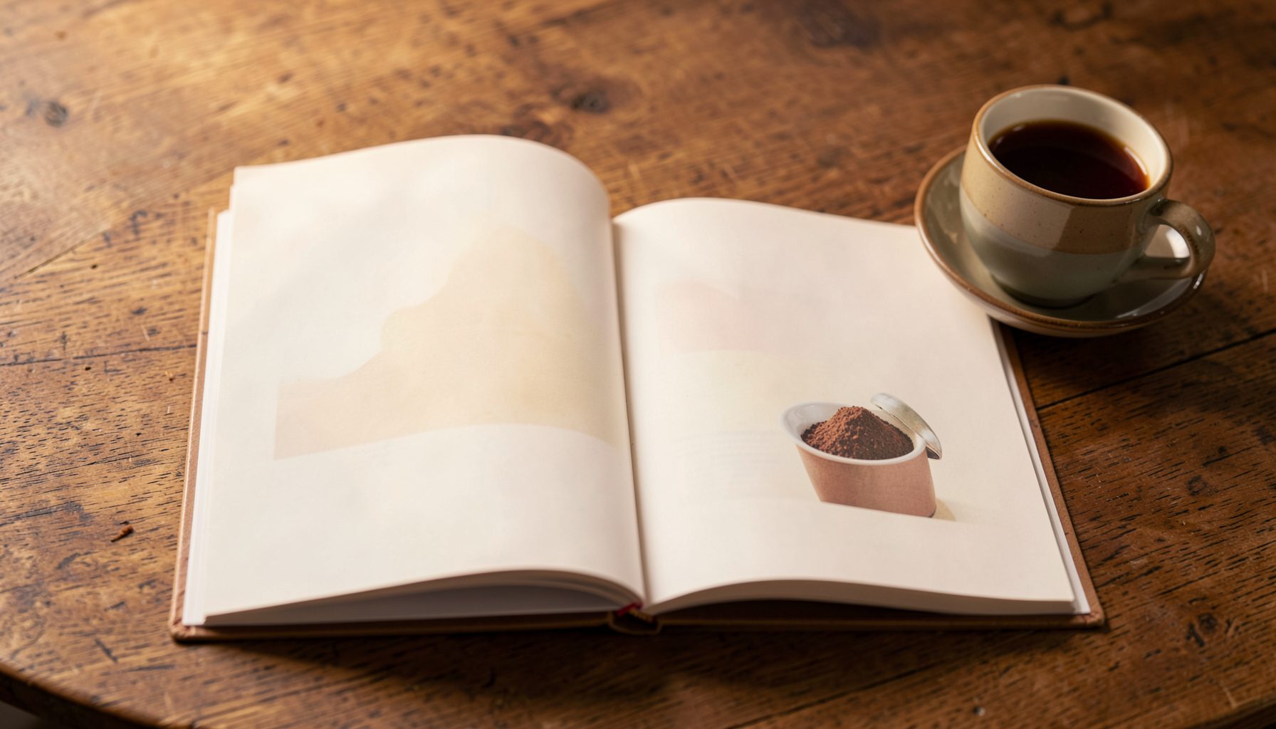 Offenes Fotobuch auf einem Holztisch mit warmem Licht, daneben eine Tasse Kaffee, sanfte Cremetöne und Braun