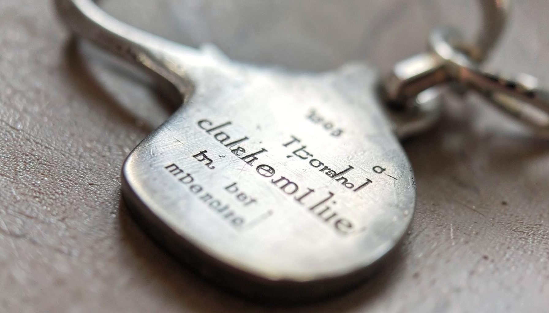 Eine Nahaufnahme eines gravierten Metallanhängers mit feiner Schrift, das Licht spiegelt sich sanft auf der Oberfläche